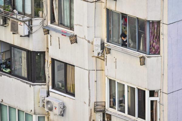 Женщина выглядывает из квартиры во время блокировки COVID-19 в районе Цзинъань в Шанхае 9 апреля 2022 года. (Hector Retamal/AFP via Getty Images)