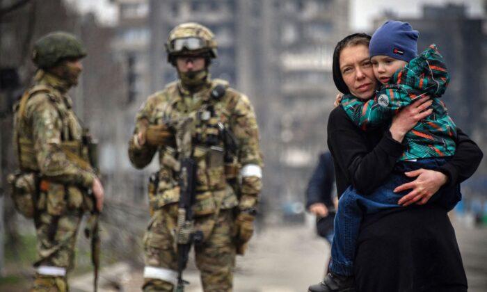 Женщина с ребёнком рядом с российскими солдатами на улице Мариуполя, 12 апреля 2022 года. Фото: Александр Неменов/AFP через Getty Images
 | Epoch Times Media
