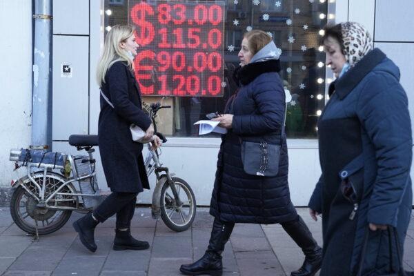 Люди на фоне экрана пункта обмена валюты, где отображается курс доллара США и евро к российскому рублю в Москве, 28 февраля 2022 года. (Pavel Golovkin, File/AP Photo)