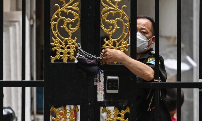 Сотрудник службы безопасности запирает дверь на цепочку в районе Цзинъань в Шанхае, где действует режим COVID-19, 2 июня 2022 года. (Hector Retamal/AFP via Getty Images)
 | Epoch Times Media