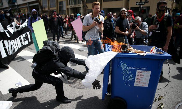 Член радикального движения «Антифа» толкает мусорный бак в сторонников Трампа во время митинга за свободу слова в Беркли. Калифорния, 15 апреля 2017 года. (Elijah Nouvelage/Getty Images) | Epoch Times Media